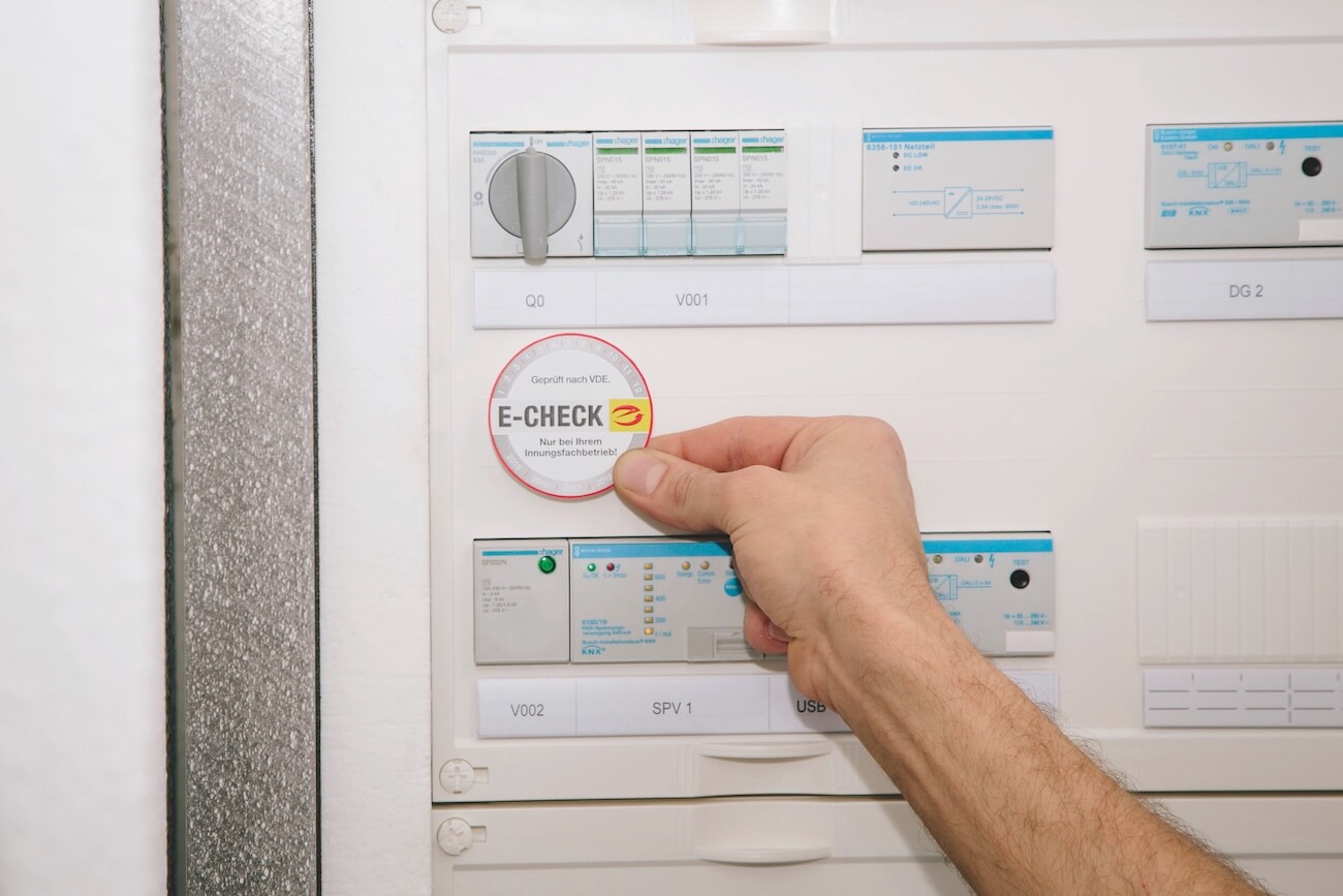 Abbildung zeigt Sicherungskasten in den gerade eine E-Check-Plakette eingeklebt wird